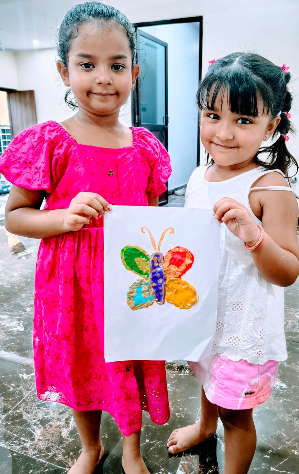 Two young Activity Zone students proudly holding a colourful hand-painted butterfly artwork from the art & craft session