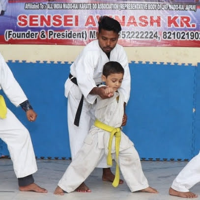 Young Activity Zone karate student in white gi with yellow belt practising stance with sensei
